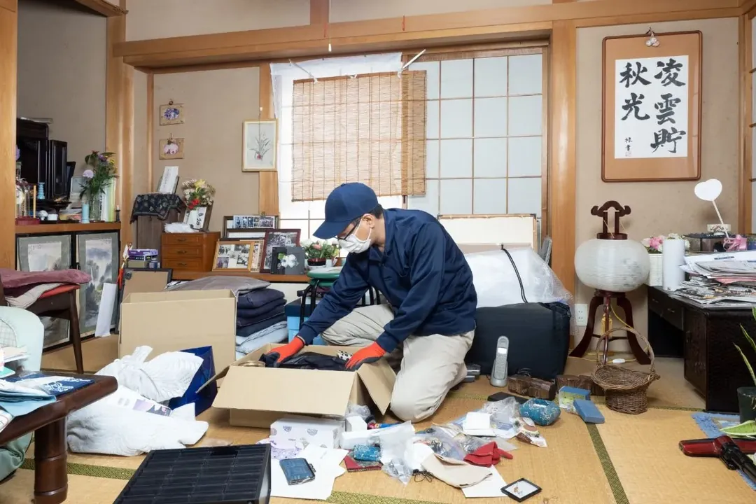 和室で遺品を一点ずつ仕分けする作業員